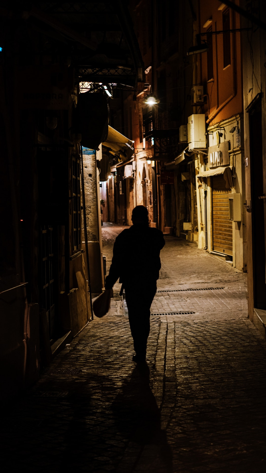 A silhouetted man walking down a lamplit alley at night